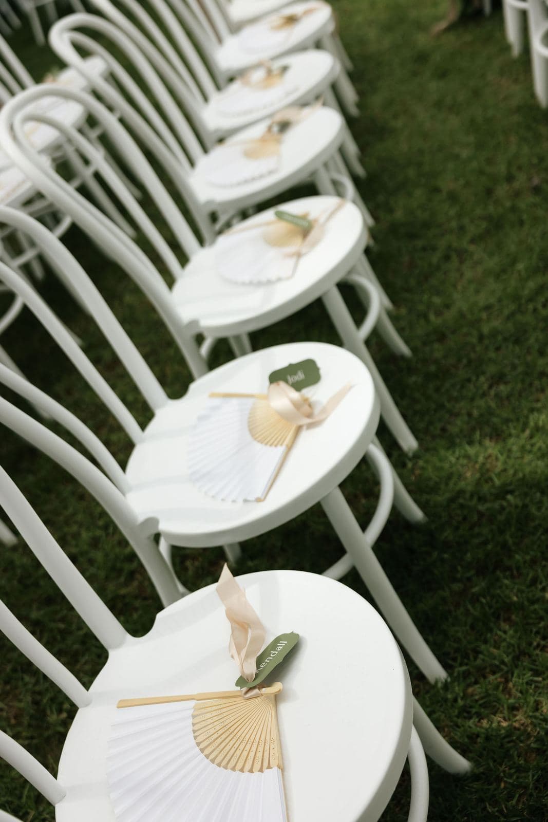 Row of white bentwood chairs with paper fans on each seat